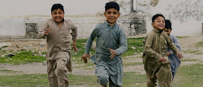 Boys in traditional Apkistani clothing in a rural setting running towards the camera