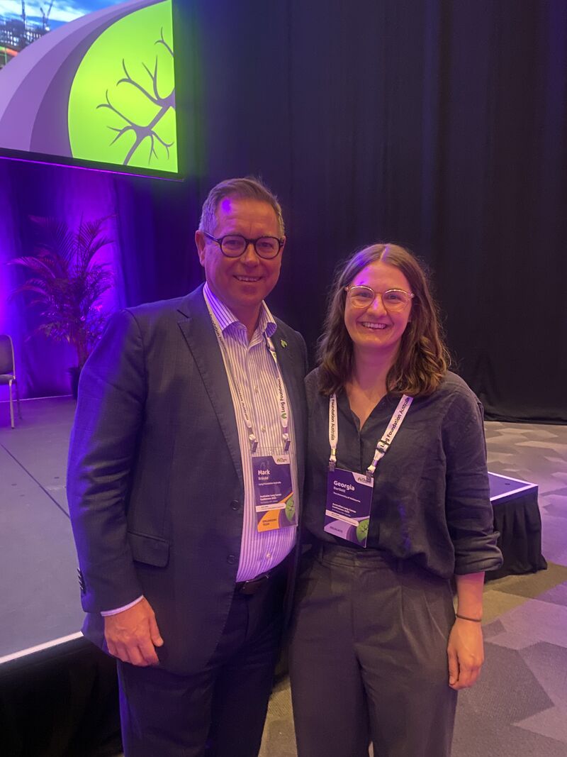 Mark Brooke and Georgia Bartlett stand side by side in front of the stage at the Australia Lung Cancer Conference 2025