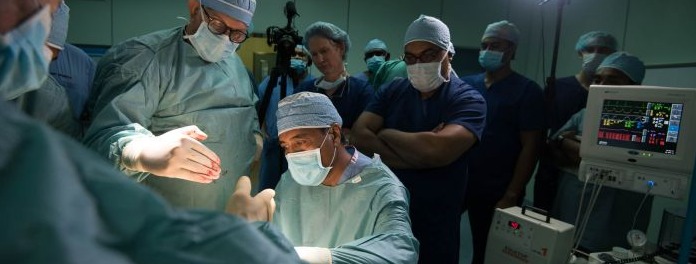 A surgical Theatre with twomen operating and a group other surgeons watching
