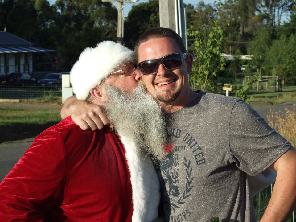 Santa embraces man in sunglasses