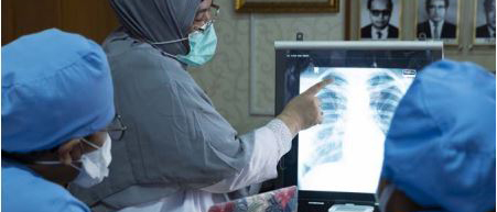 Three people in medical scrubs looks at an Xray of a chest with Tuberculosis