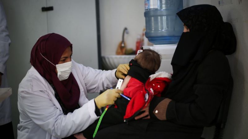 Female Doctor in a hijab gives an injection to a child being held by female in a burqa