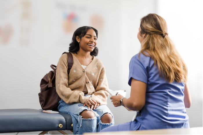 Young adult female smiles in conversation with the unrecogniseable nurse stock photo