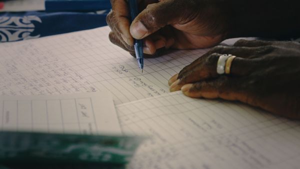 Close up of brown pacific islander hands writing in a note book ut vaccination paperwork at the rural hospital clinic