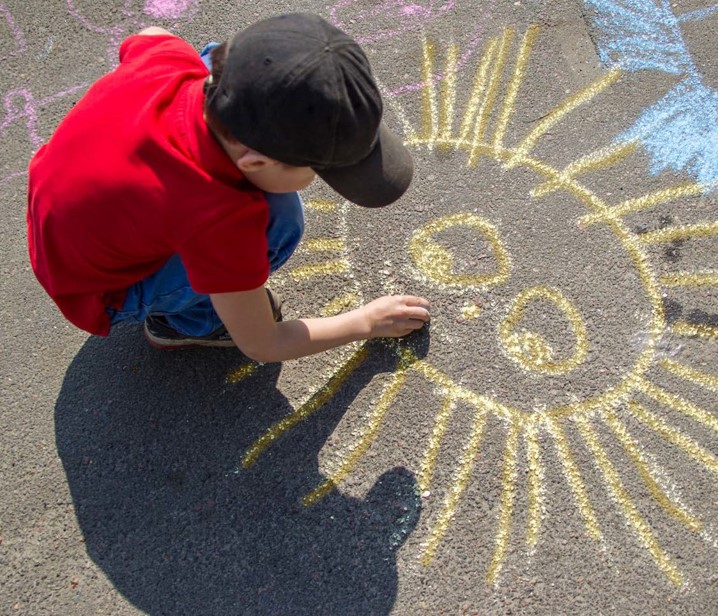 Photo of child drawing a smiling sun with chalk on concrete